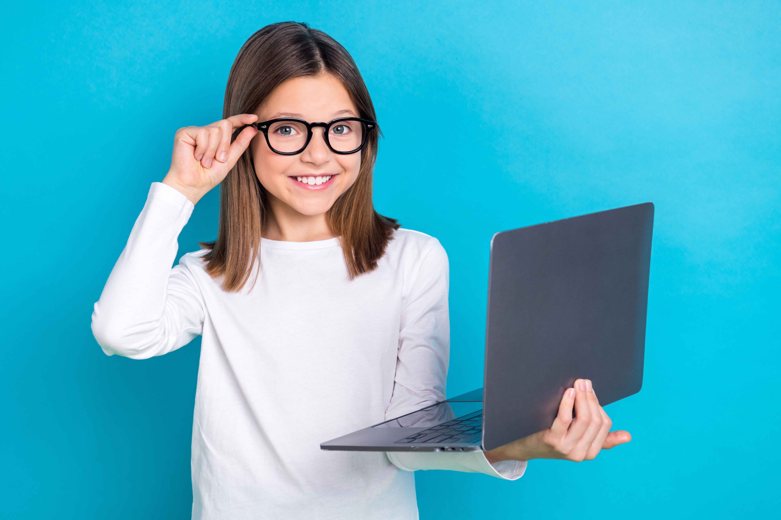 Photo of cheerful satisfied girl with long hairstyle wear white long sleeve touching glasses hold laptop isolated on blue color background.