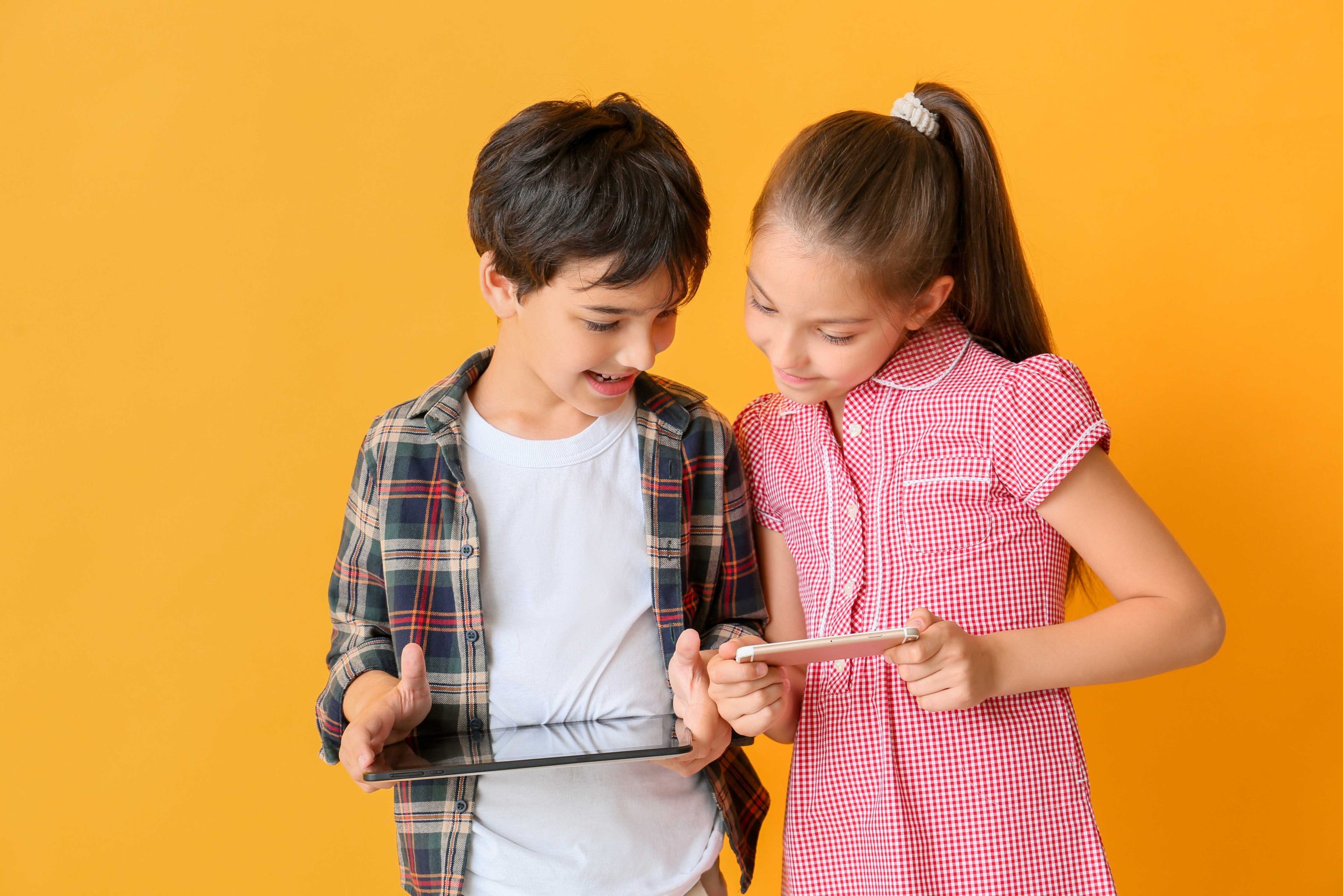 Cute little children with tablet computer and mobile phone on color background